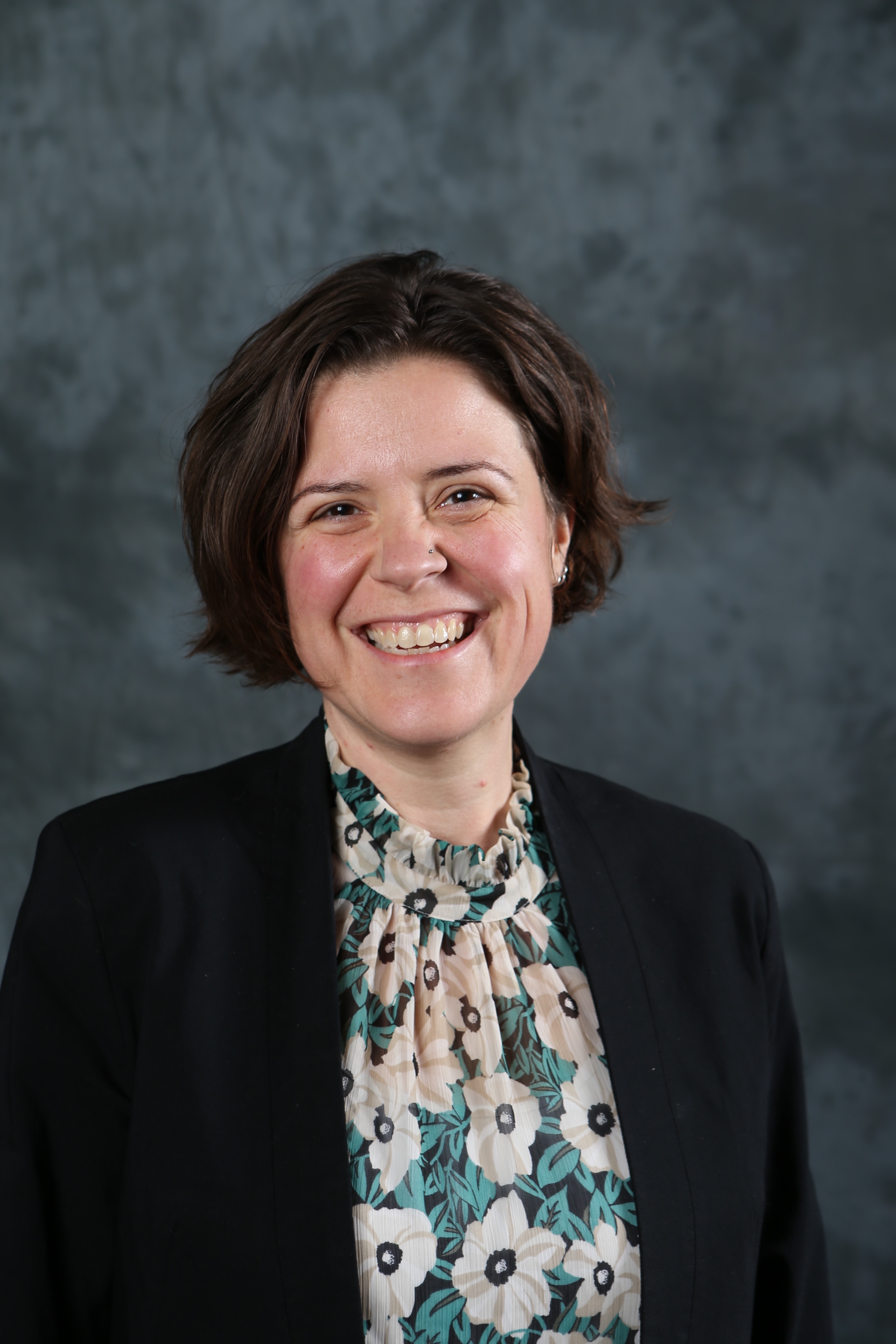 Woman with dark hair and dark blazer smiles.