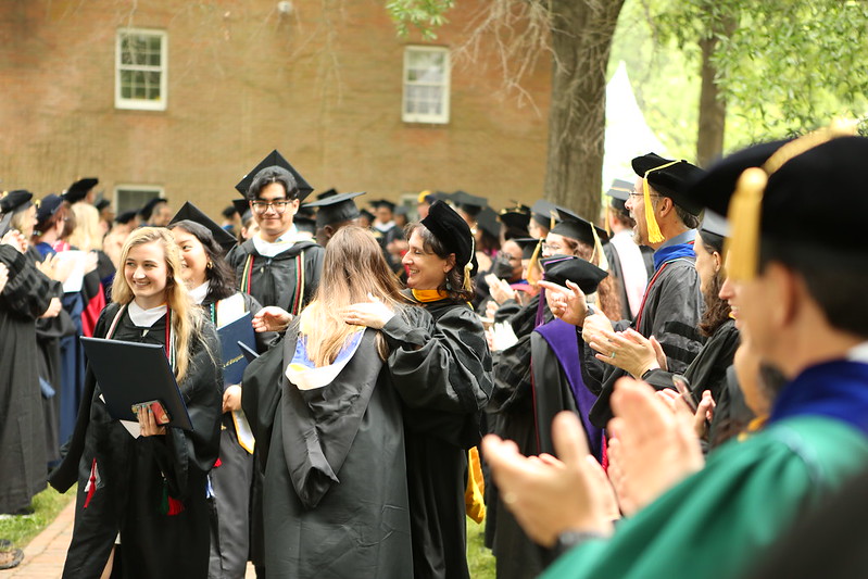 Graduates in caps and gowns celebrate outdoors, receiving diplomas and congratulations from faculty during a graduation ceremony.