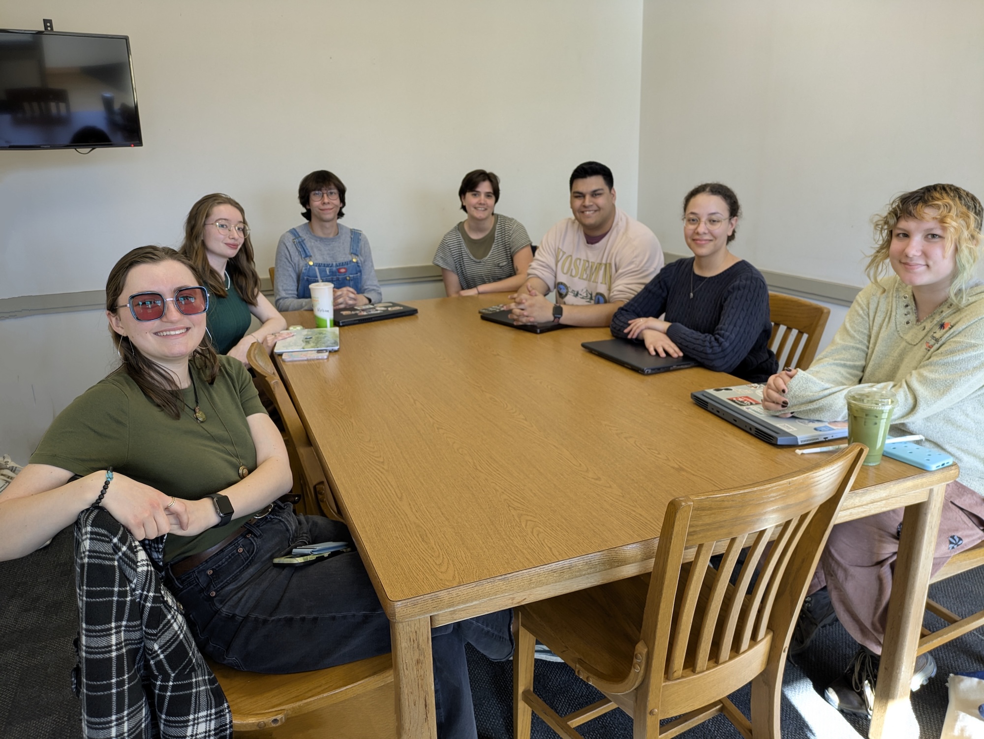 Seven people sitting around a wooden table in a meeting room, smiling at the camera.