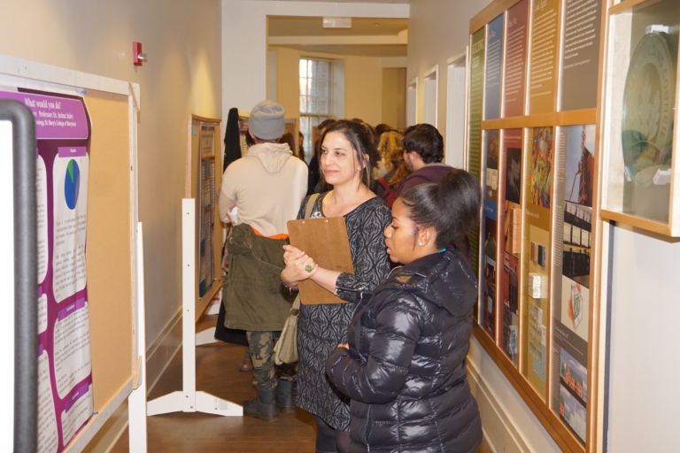 People stand in a hallway, observing and discussing educational posters displayed on bulletin boards along the walls.