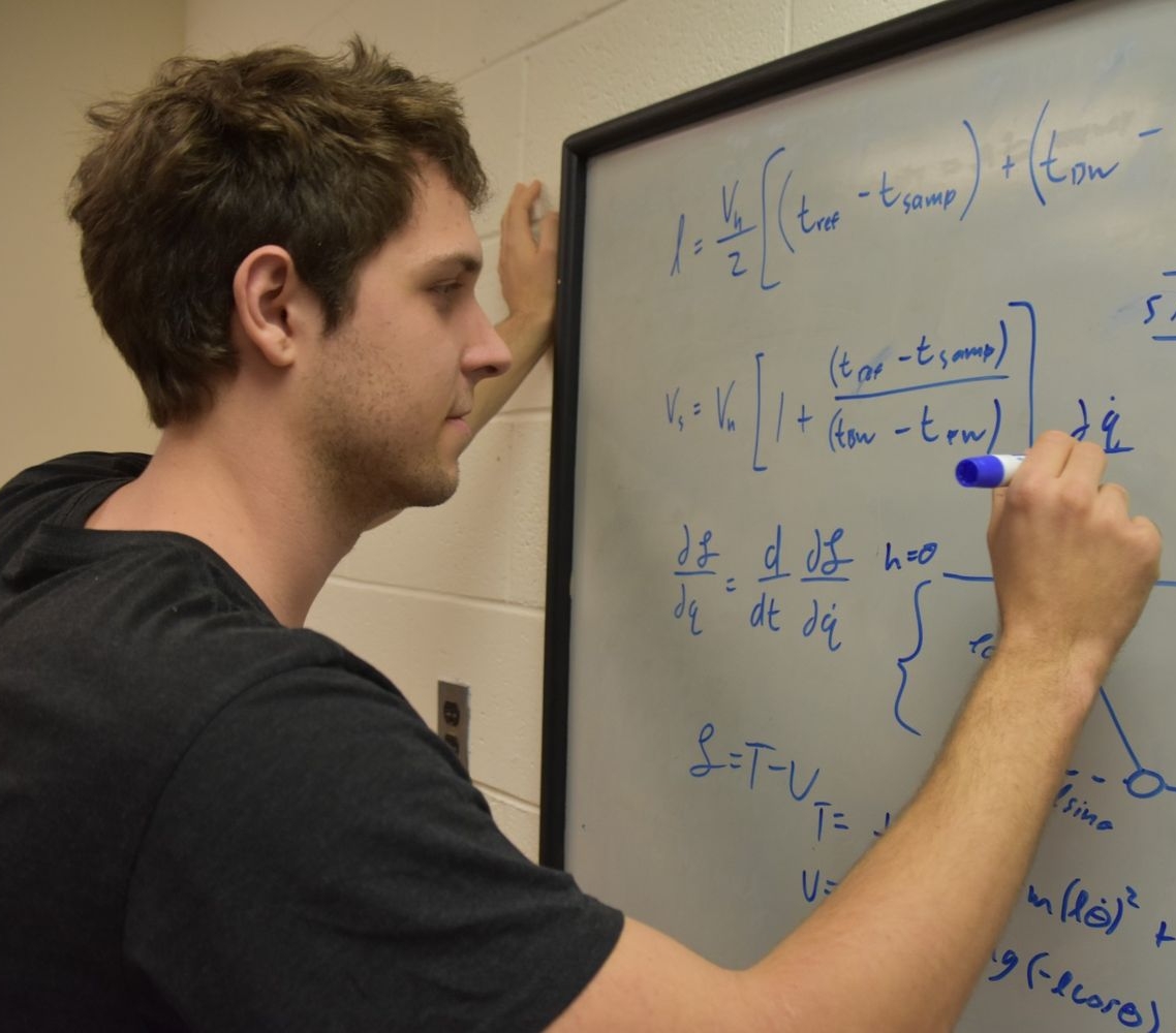 A person writes mathematical equations on a whiteboard with a blue marker in a classroom or office setting.