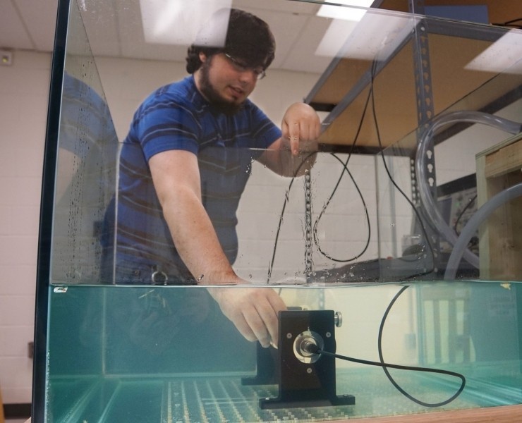 A person in a blue striped shirt adjusts equipment inside a large water tank in a laboratory setting.
