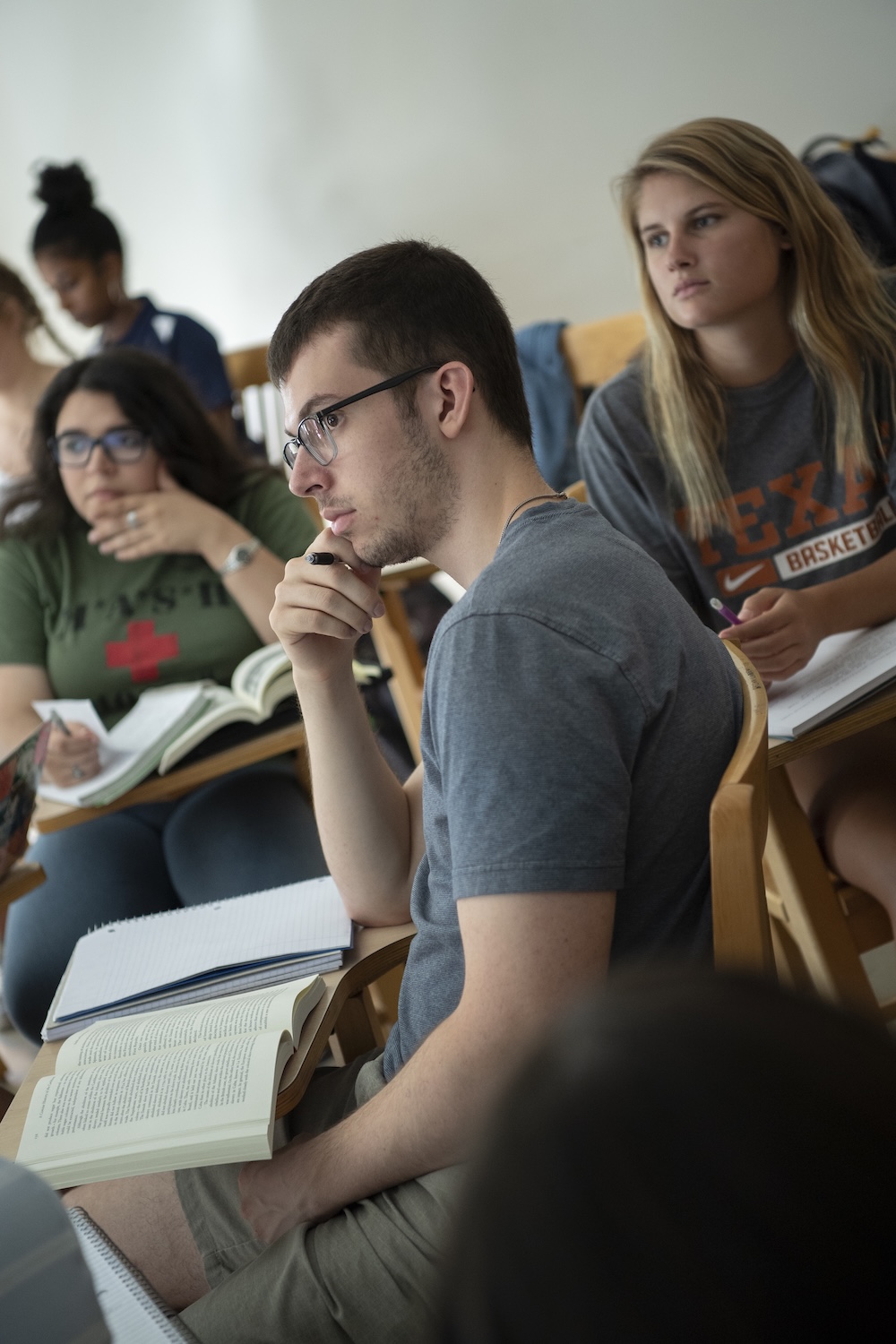 Students sitting in a classroom, attentively listening and taking notes, with open books and notebooks in front of them.