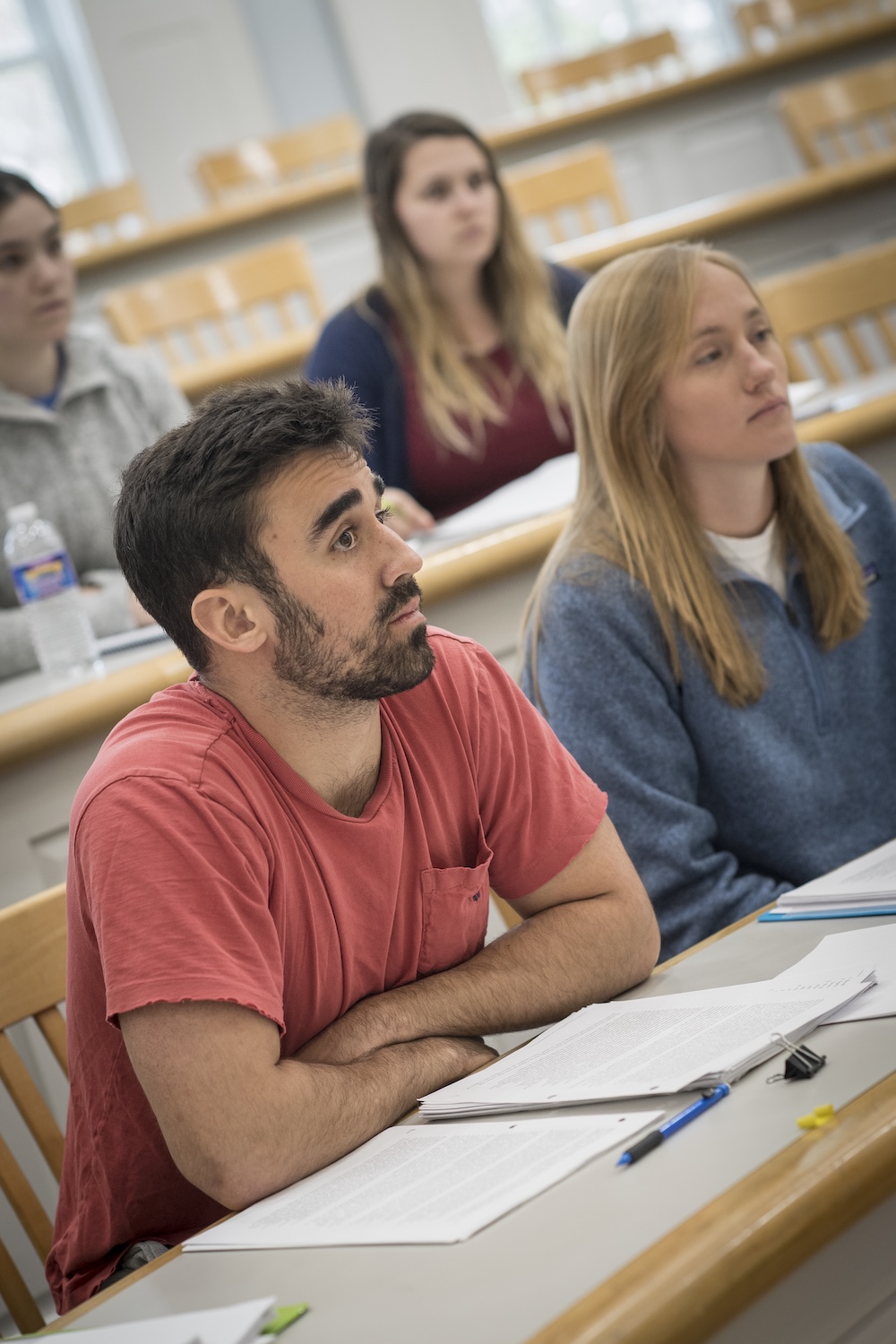 A group of students sit at desks in a classroom, attentively listening and taking notes during a lecture.