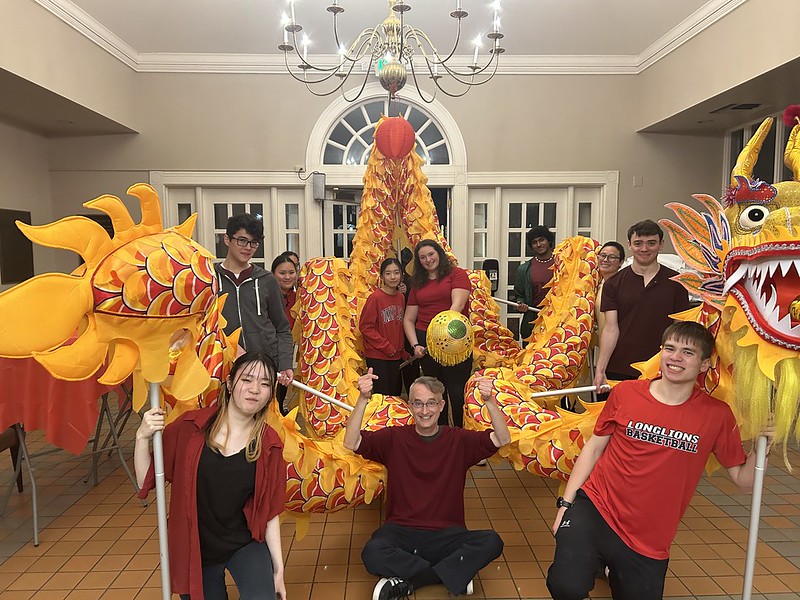 A group of people poses indoors with a brightly colored dragon costume, commonly used in traditional dragon dance performances.