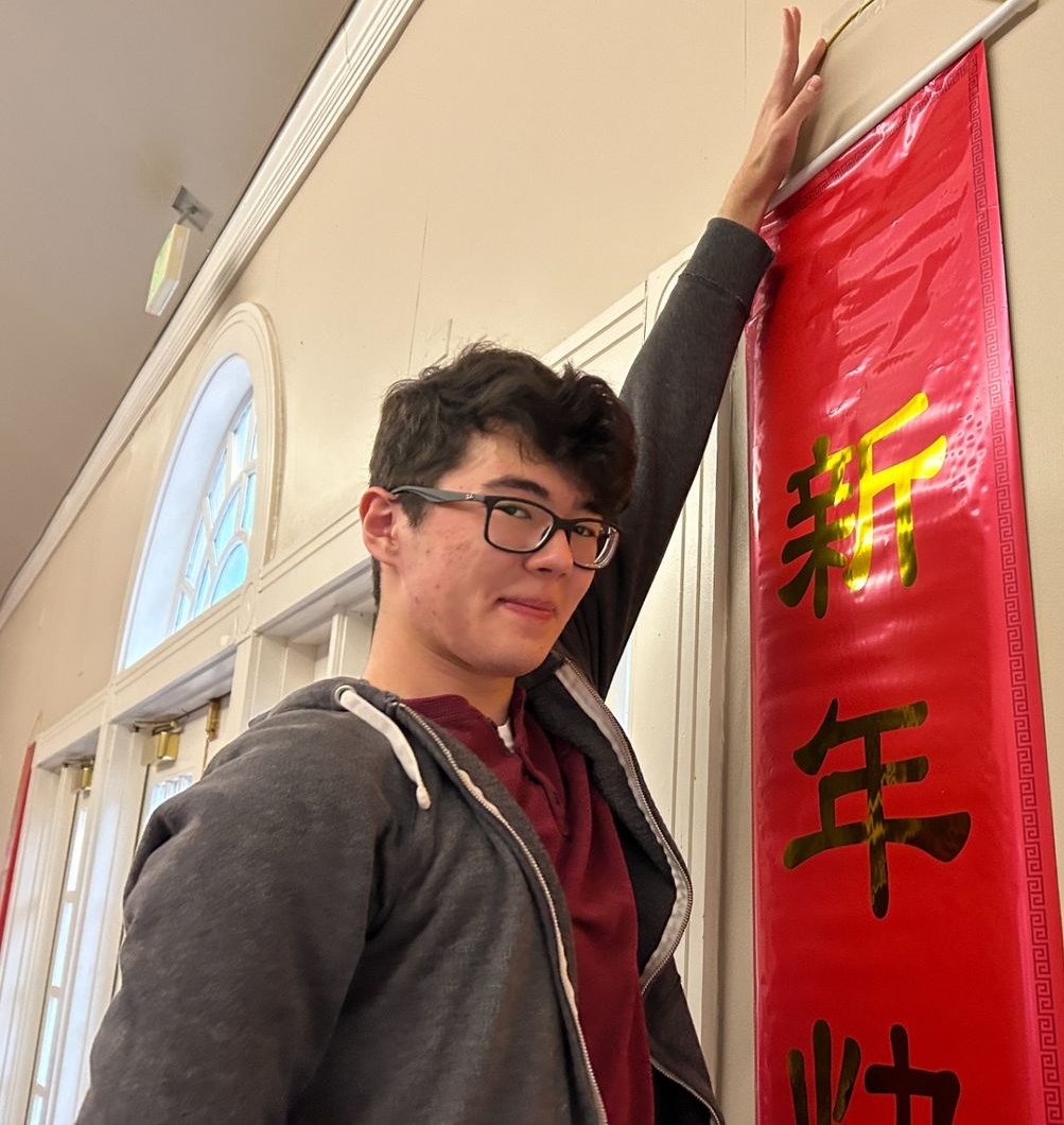 A person stands indoors, touching the top of a red vertical banner with 中国 characters hanging on a beige wall.