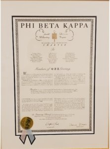A framed Phi Beta Kappa honor society certificate with decorative borders and a gold seal. The text refers to the society's history, purpose, and membership recognition. A ribbon is attached at the bottom.